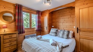 Un dormitorio de cabaña de madera con una cama, un aparador, un espejo y una ventana con cortinas.