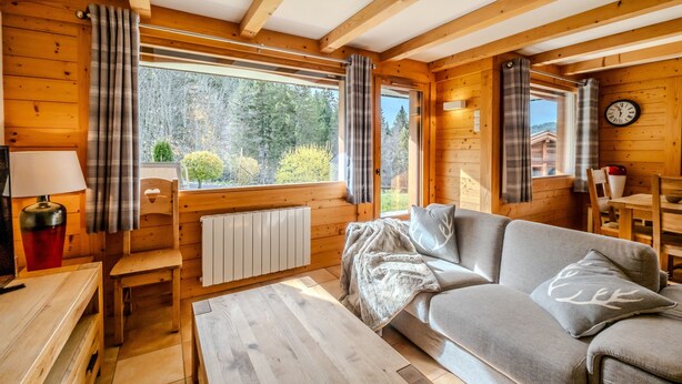 Interior acogedor de una cabaña con paredes de madera, un sofá, una mesa y una ventana con cortinas.