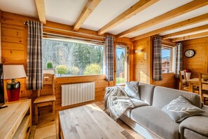 Interior acogedor de una cabaña con paredes de madera, un sofá, una mesa y una ventana con cortinas.