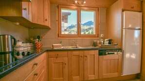 Una cocina con armarios de madera, una tetera de acero inoxidable, una cafetera y vistas a montañas a través de una ventana.