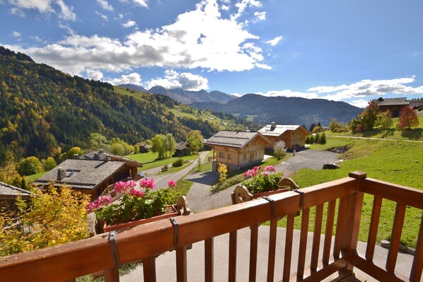 A scenic view of a village with traditional houses, a wooden balcony, and a clear sky.