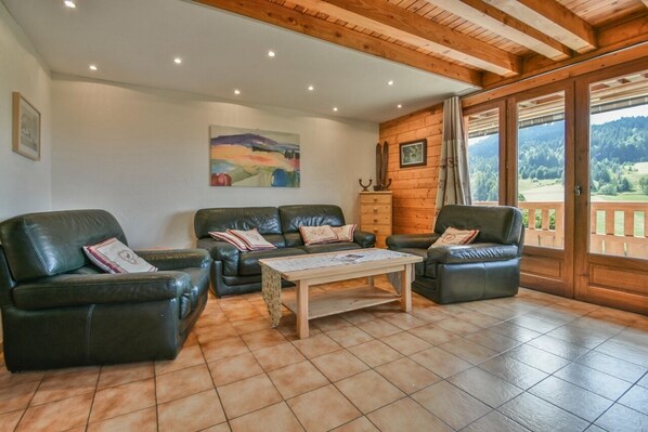 A cozy living room with leather sofas, a wooden coffee table, and a large window offering a scenic view.