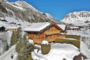 Un chalet en bois doté d’un balcon, entouré de montagnes et d’arbres couverts de neige.
