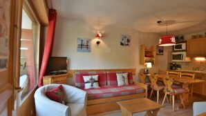 A cozy living room with a sofa, a television, and a dining area with wooden furniture.