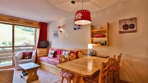 A cozy room with a wooden dining table, a sofa, a TV, and a window with a red curtain.