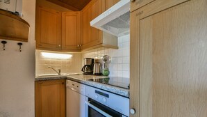 A compact kitchen with wooden cabinets, a built-in oven, and a coffee maker. - Refuge Le Bardeau B4 (Le Grand Bornand)