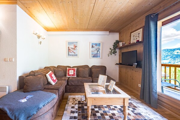 Un salon chaleureux avec un plafond en bois, un canapé en cuir marron, une table basse et une vue sur un paysage enneigé par la fenêtre.