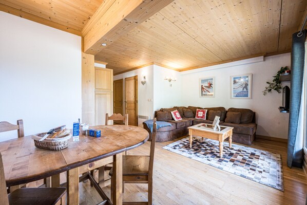 A cozy living room with a wooden ceiling, a dining table with chairs, a sofa, and a coffee table.