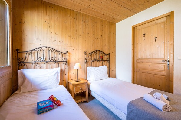 Una habitación con dos camas individuales, paredes y puerta de madera, y una mesita de noche pequeña con una lámpara.