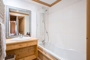 Une salle de bain avec un meuble-lavabo en bois, un grand miroir, une baignoire et une douche.