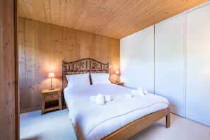 Une chambre à coucher avec une tête de lit en bois, deux tables de chevet avec des lampes, un lit avec du linge de lit blanc et une grande armoire.