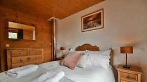 A wooden cabin-style bedroom with a bed, pillows, a nightstand, a mirror, and a framed picture on the wall. - Chalet Mitoyen - Rosa (Le Grand Bornand)