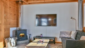 A cozy living room with a fireplace, a flat-screen TV mounted on the wall, a sofa, and a coffee table. - Chalet Mitoyen - Rosa (Le Grand Bornand)