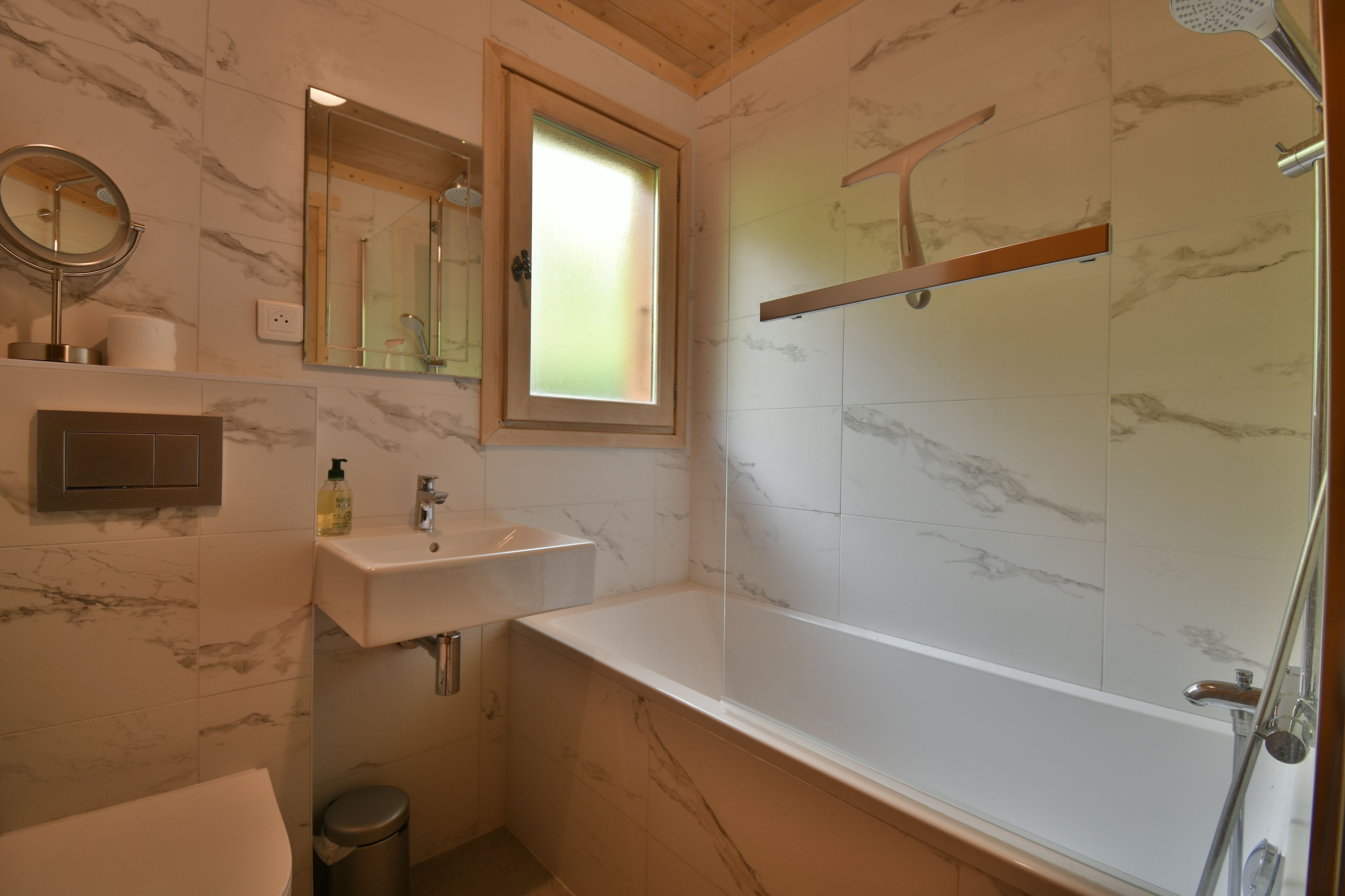 A bathroom with a marble-tiled shower, a glass-enclosed bathtub, a sink with a mirror, and a window.