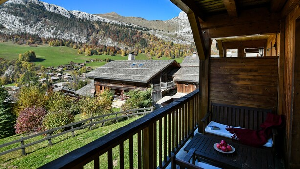 Un balcón de madera con vistas a un pueblo de montaña, un banco de madera y un plato de manzanas.