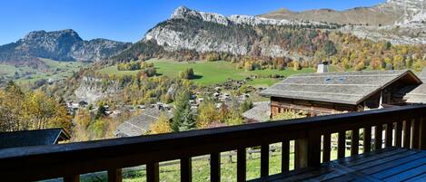 Une terrasse en bois offrant une vue panoramique sur un paysage montagneux, avec un village situé en contrebas.