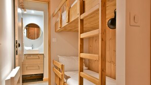 Habitación pequeña con literas, un armario de madera, un espejo redondo y un lavamanos.