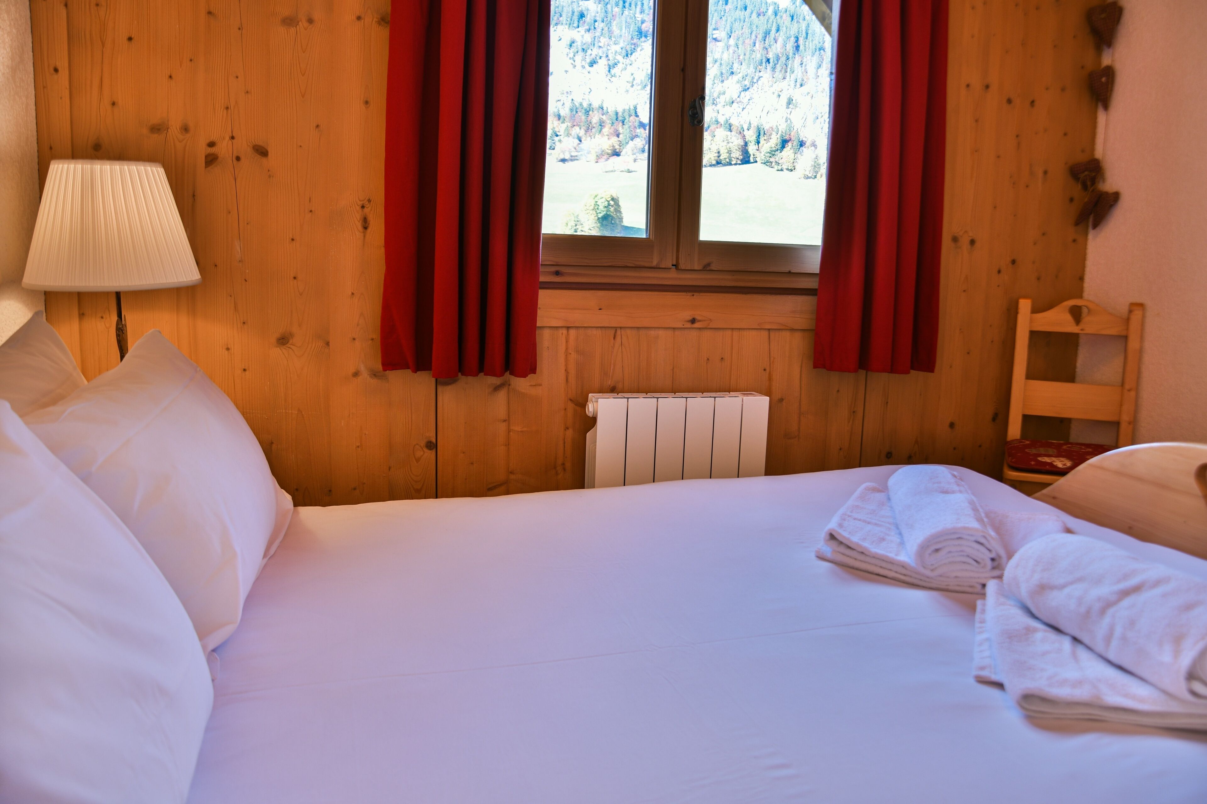 A wooden-paneled room with a bed, a radiator, and a window with red curtains.