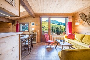 A wooden interior with a dining area, a sofa, and a view of a green landscape.