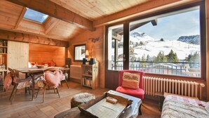 Un interior de madera acogedor con comedor, un sofá rojo y un amplio ventanal con vistas a una montaña nevada.