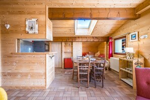 A wooden cabin interior with a dining area, kitchen, and a cozy seating space.