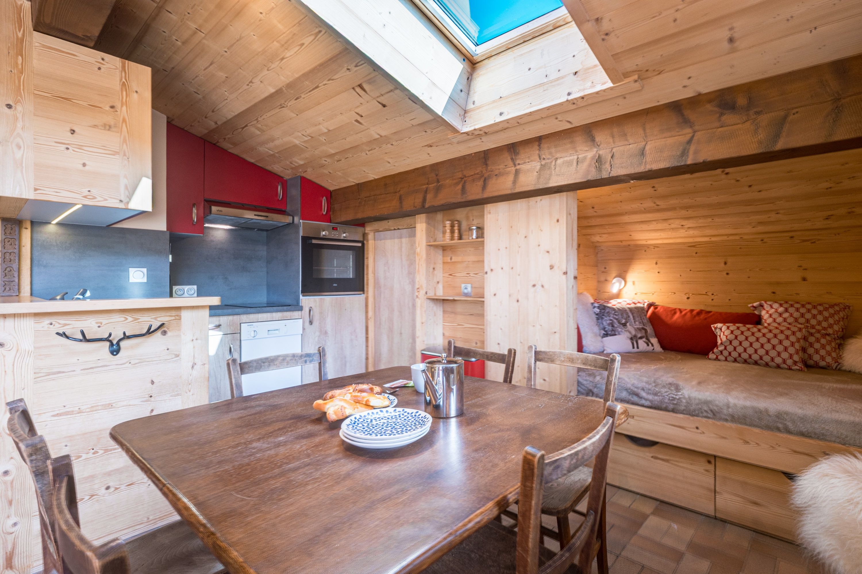 A cozy cabin interior with a wooden dining table, chairs, a kitchenette, and a sofa bed.
