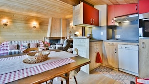 Una habitación acogedora de estilo cabaña con techo de madera, un comedor con mantel a cuadros, una cama con edredón escocés y una kitchenette con armarios rojos y un refrigerador de acero inoxidable.