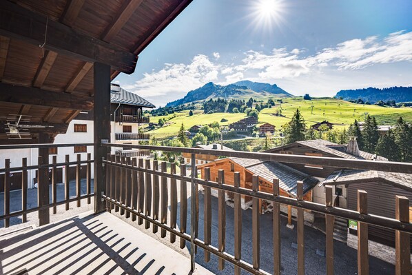 A wooden balcony with a view of a mountainous landscape and traditional buildings.