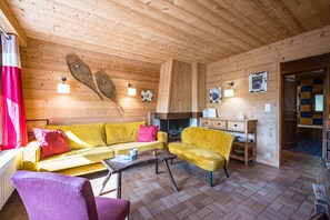 A cozy wooden interior with a sofa, armchair, and a fireplace.