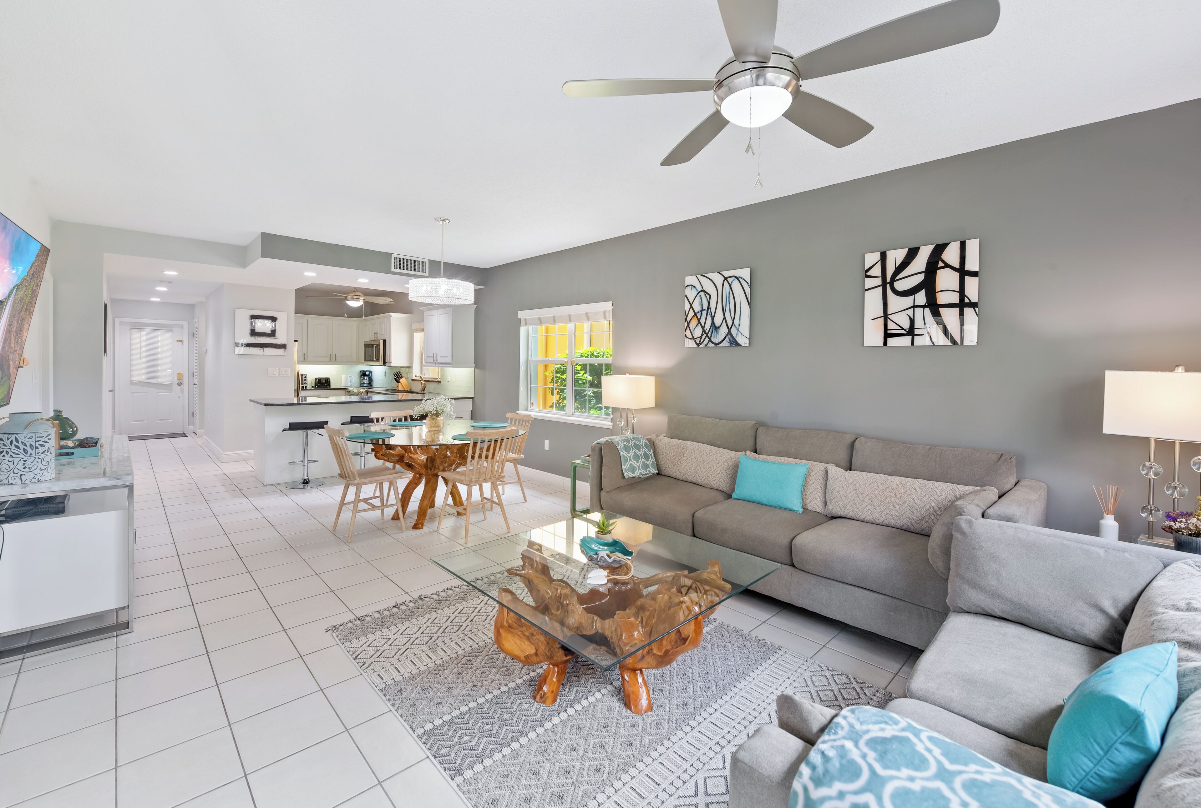 A modern living room with a glass coffee table, grey sofa, and a dining area with wooden chairs.