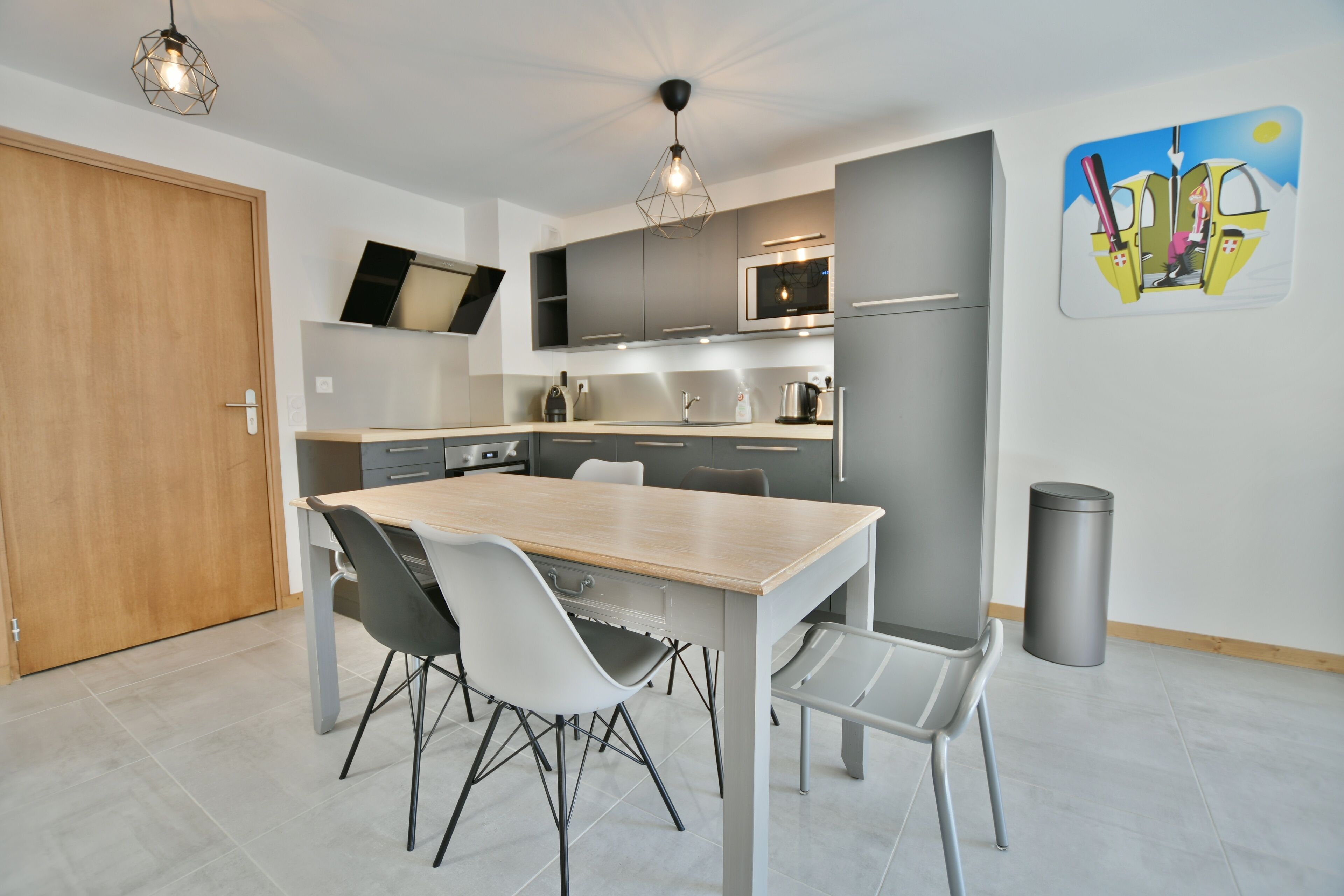 Una cocina moderna con armarios grises, una mesa de comedor de madera y sillas blancas.