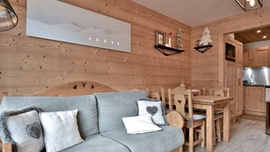 Um quarto aconchegante com um sofá cinzento, paredes de madeira, uma mesa de jantar com cadeiras e uma área de cozinha.
