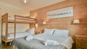Quarto com beliches, uma cama grande, paredes de madeira e uma obra de arte pendurada na parede.