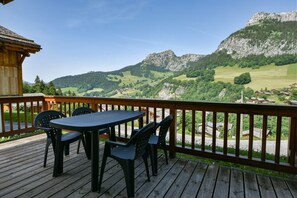 Une terrasse en bois avec une table et des chaises, offrant une vue sur un paysage montagneux.