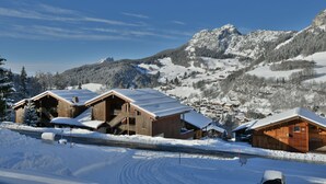 A wooden lodge with a snow-covered roof, set against a mountainous backdrop. - Refuge Le Gypaète G6 (Le Grand Bornand)