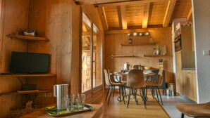 A wooden interior with a dining area, kitchen, and a television on a shelf. - Refuge Le Gypaète G6 (Le Grand Bornand)