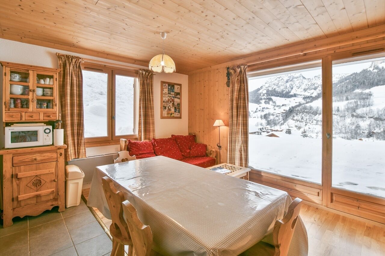 Ett mysigt rum med ett träpanelat tak, ett matbord, en soffa och stora fönster med utsikt över ett snötäckt berg.
