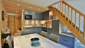 Una cocina compacta con armarios grises, una escalera de madera y un comedor con mesa y sillas.