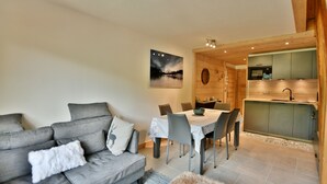 Una sala de estar moderna con un sofá gris, una mesa de comedor con sillas y una zona de cocina con armarios de madera y un lavamanos.