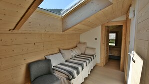 Una habitación acogedora con techo inclinado, paredes de madera, un sofá con ropa de cama a rayas y una ventana con vistas a un área boscosa.