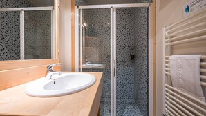 Une salle de bain avec un meuble-lavabo en bois, un lavabo blanc, une cabine de douche en verre et un porte-serviettes.