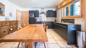Une cuisine moderne avec une table à manger en bois, des meubles de rangement sombres et une grande fenêtre.
