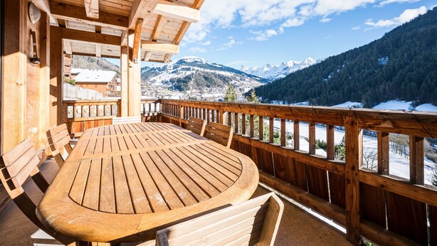 Une terrasse en bois avec une table et des chaises, offrant une vue sur un paysage montagneux enneigé.