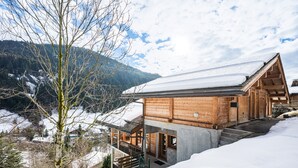 Un chalet en bois, avec un toit enneigé, un balcon et une vue sur un paysage montagneux couvert de neige.