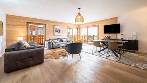 Un vaste espace de vie doté d’un plancher en bois, d’un canapé, d’une table à manger avec des chaises, d’un téléviseur et d’un balcon agrémenté d’une balustrade.