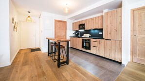 Une cuisine moderne avec des meubles en bois, un réfrigérateur noir et une table à manger en bois, accompagnée de tabourets.