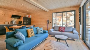 Un intérieur moderne avec un plafond en bois, un canapé avec des coussins, une table à manger et un coin cuisine.