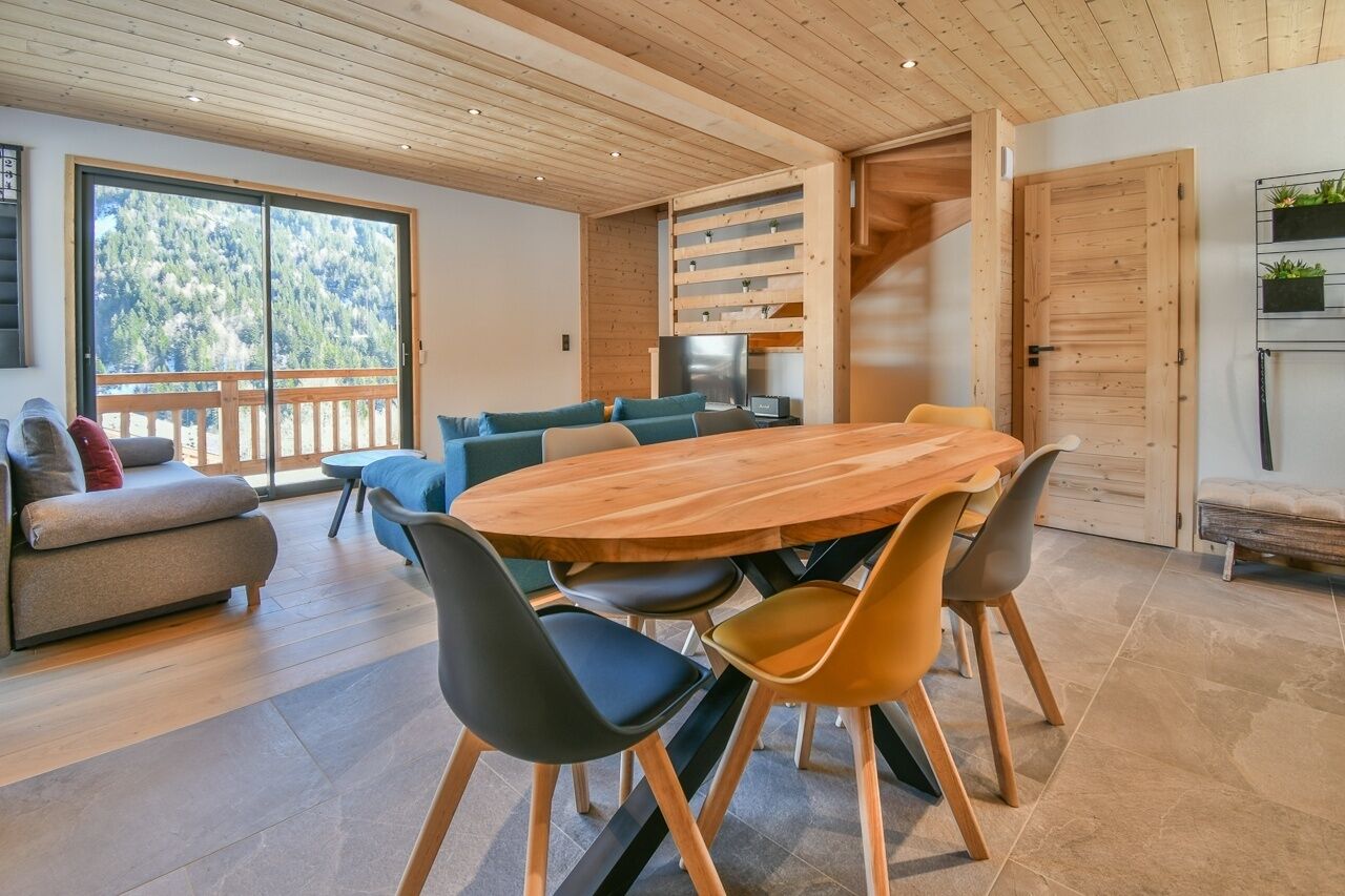 Ein moderner Essbereich mit Holztisch und -stühlen, einer Couch und einer Treppe, die in eine obere Ebene führt.