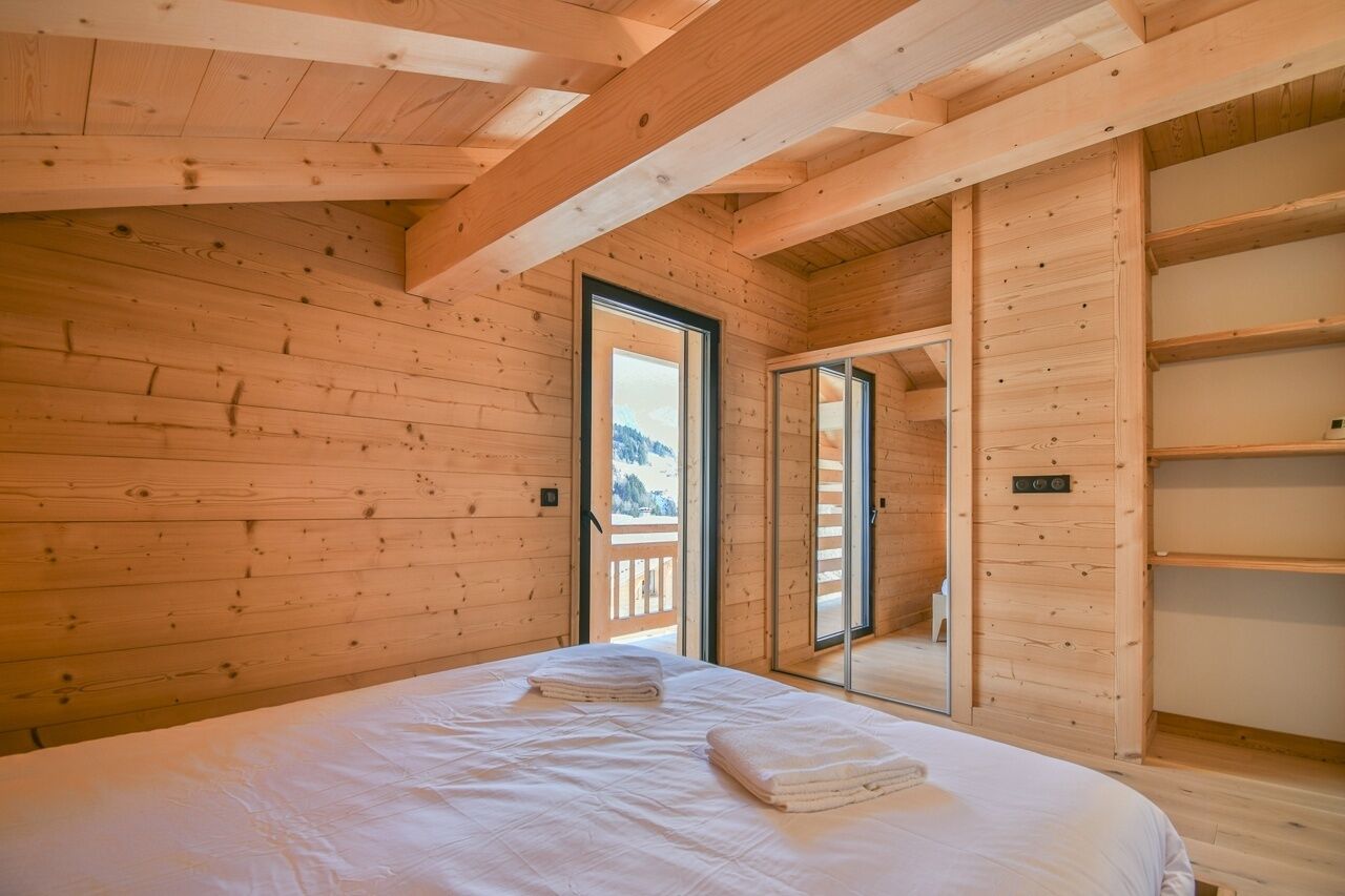 Et træhusværelse med en seng, en skydedør til en balkon og en reol i træ.