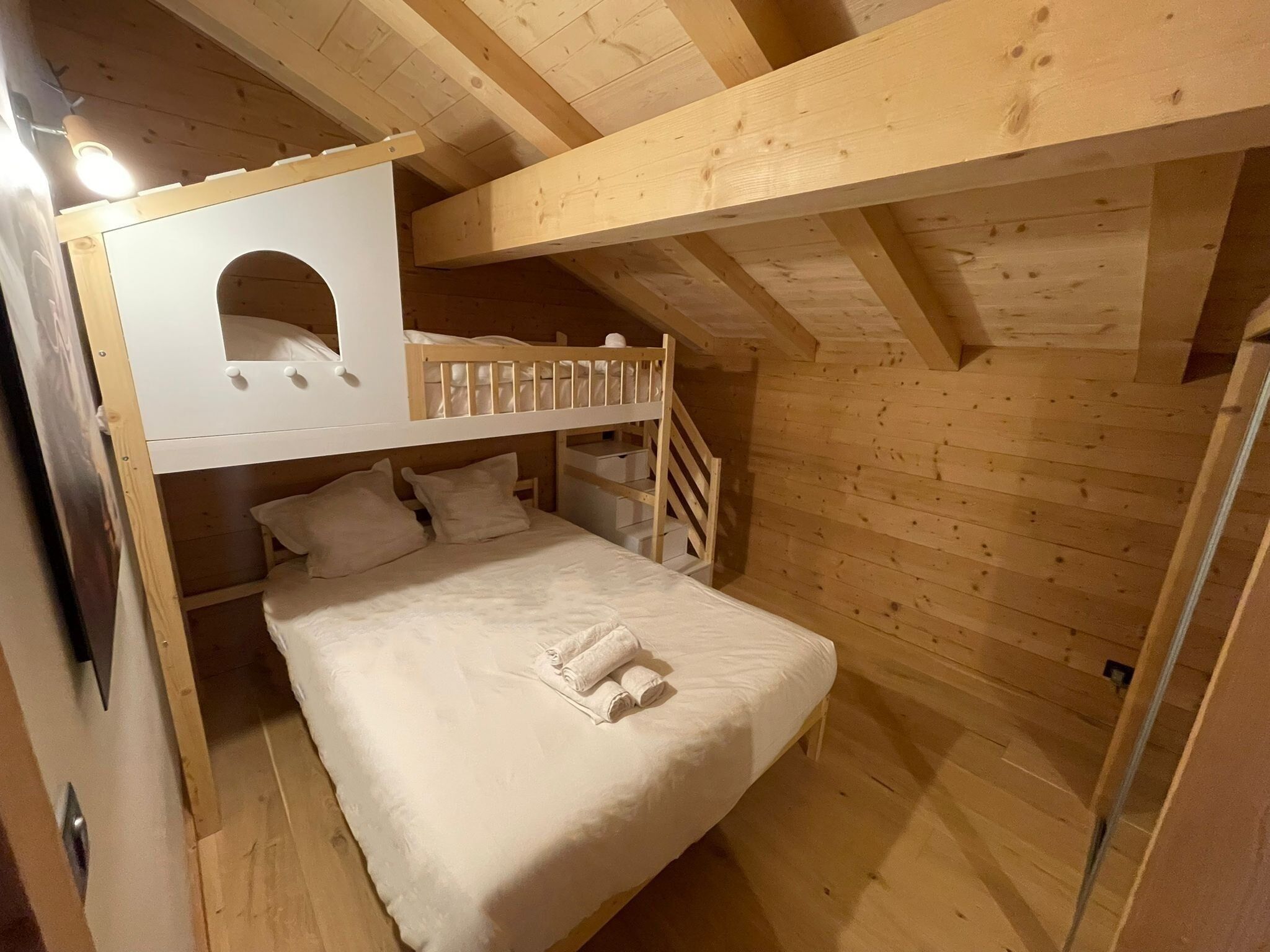 A wooden cabin with a bunk bed, a small desk, and a ladder.